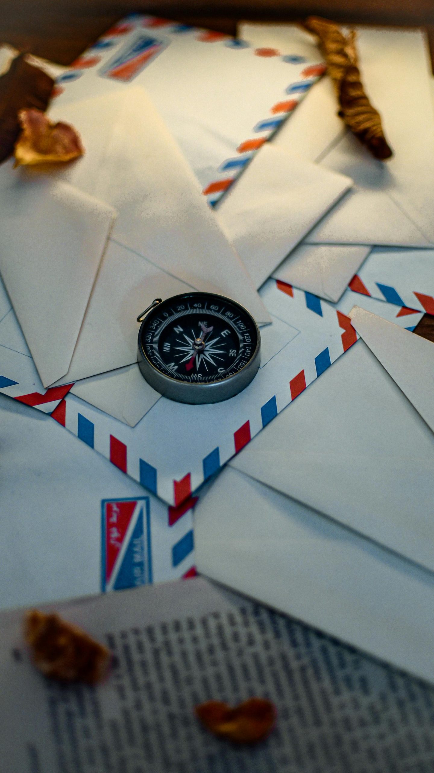 A compass placed on a stack of airmail envelopes with dried leaves, suggesting exploration or travel.